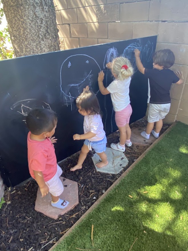 Children drawing on an outdoor chalkboard